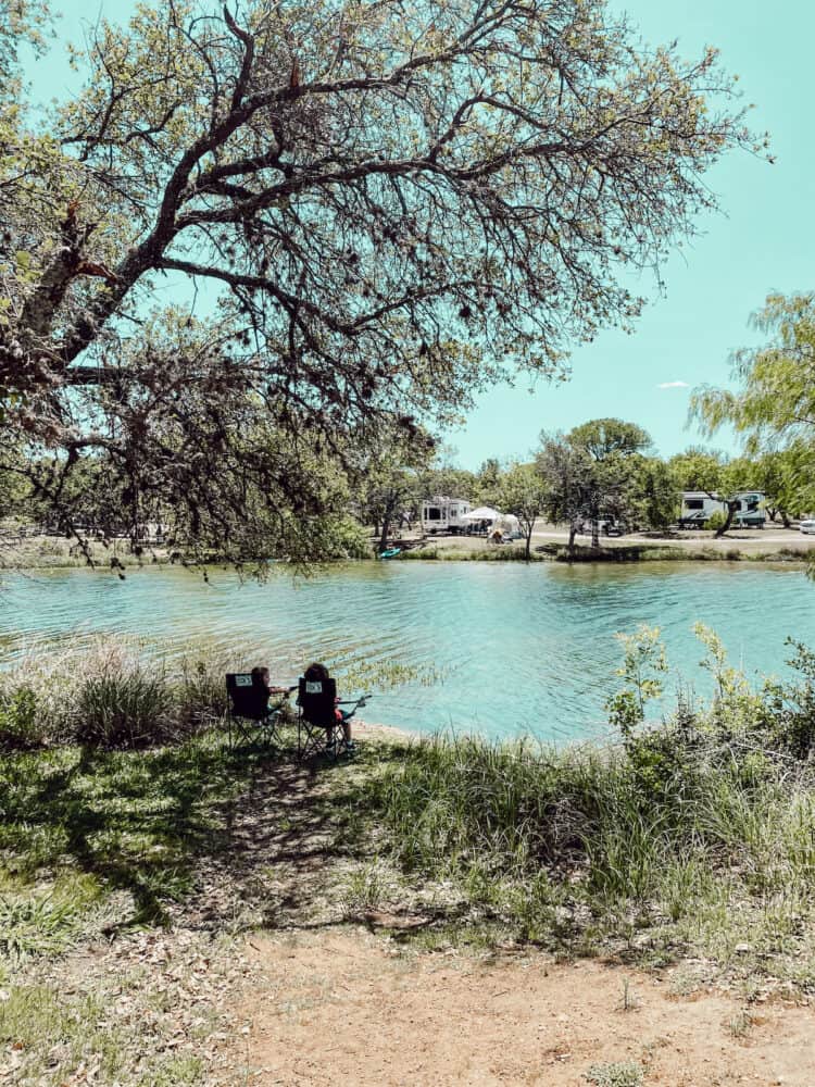 two boys sitting in camping chairs in front of a lake
