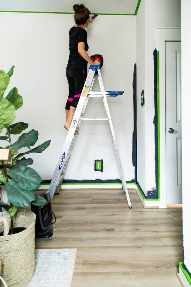 woman painting a room, with the baseboards and ceiling taped off with painter's tape