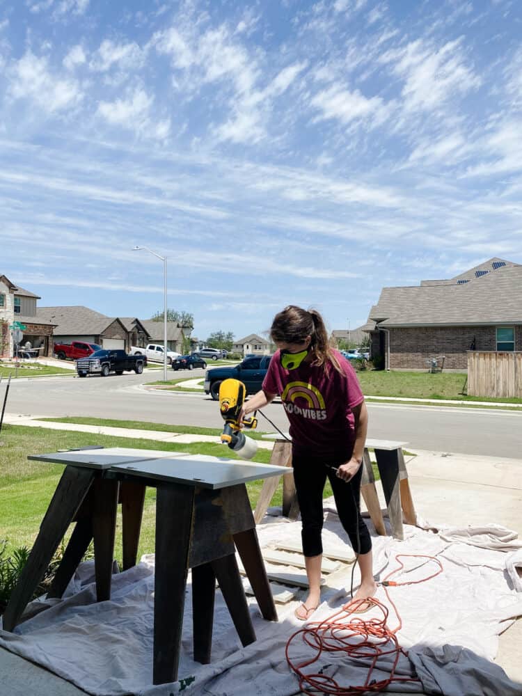 woman using a paint sprayer on cabinet doors 
