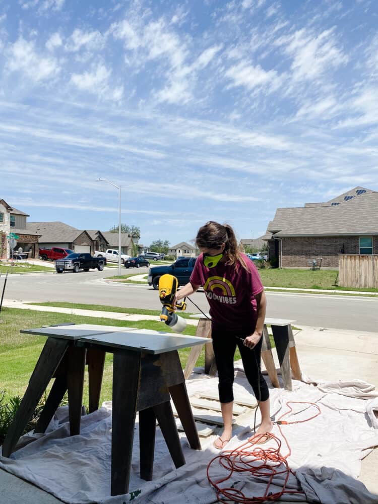 woman using a paint sprayer to paint vanity cabinets