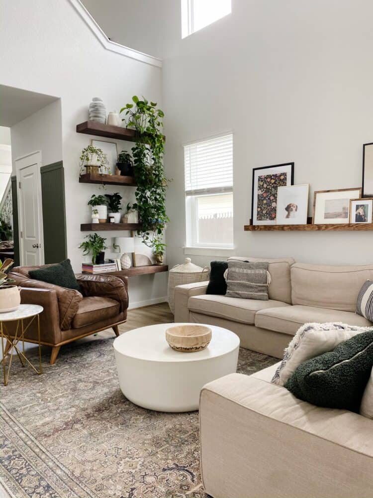 living room with a neutral color palette, floating shelves with lots of plants, and a large basket for throw blankets 