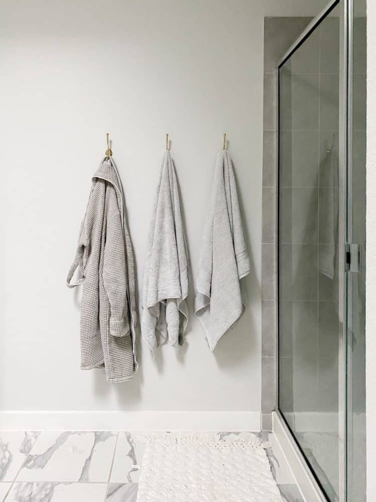 a white and gray bathroom with gold towel hooks hanging on the wall 