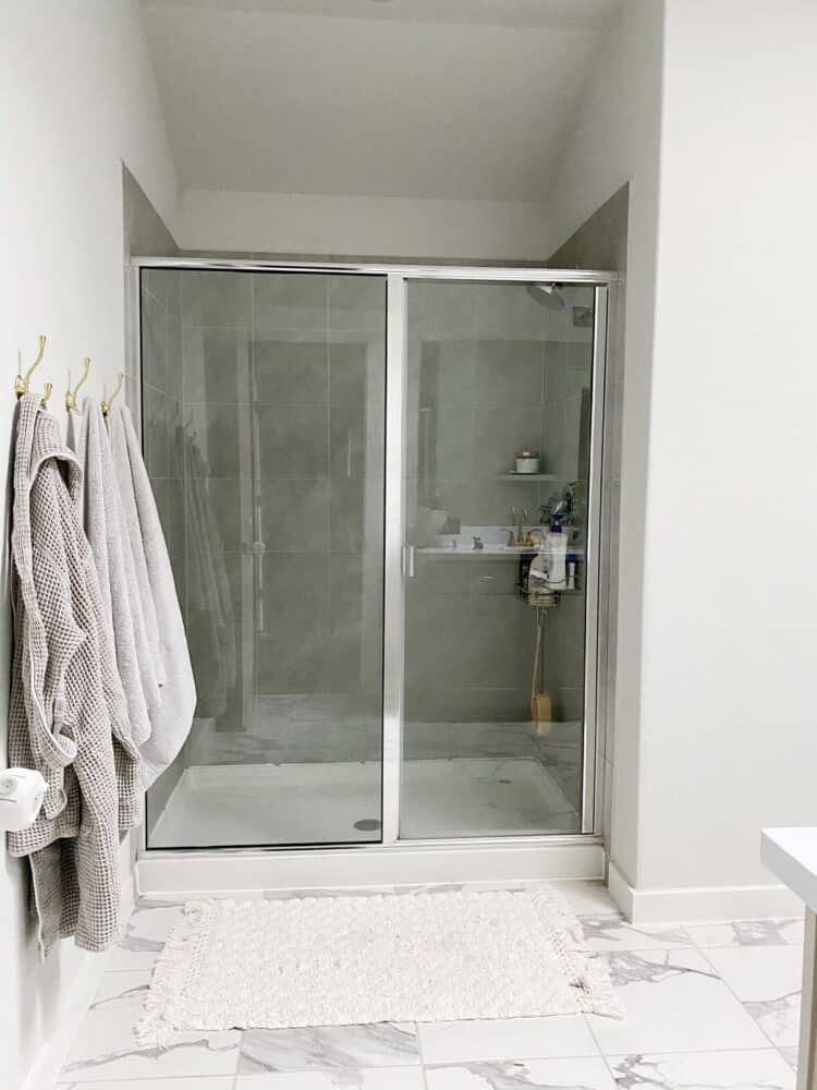 gray shower in a neutral bathroom with three gold towel hooks hanging on the wall 