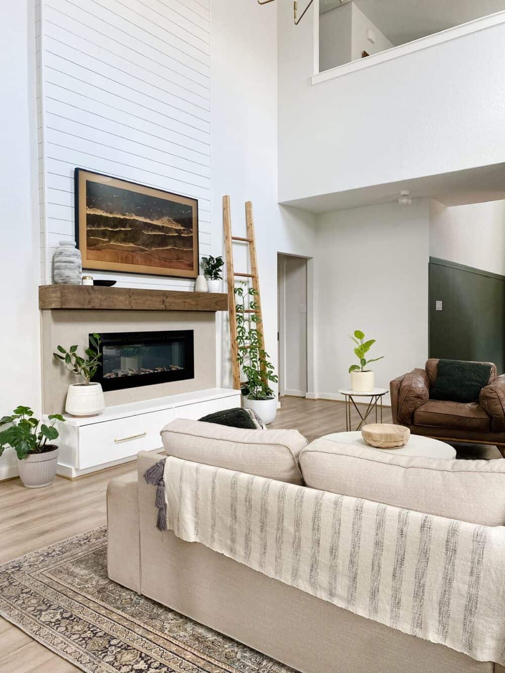 Neutral living room with tall fireplace and lots of plants 