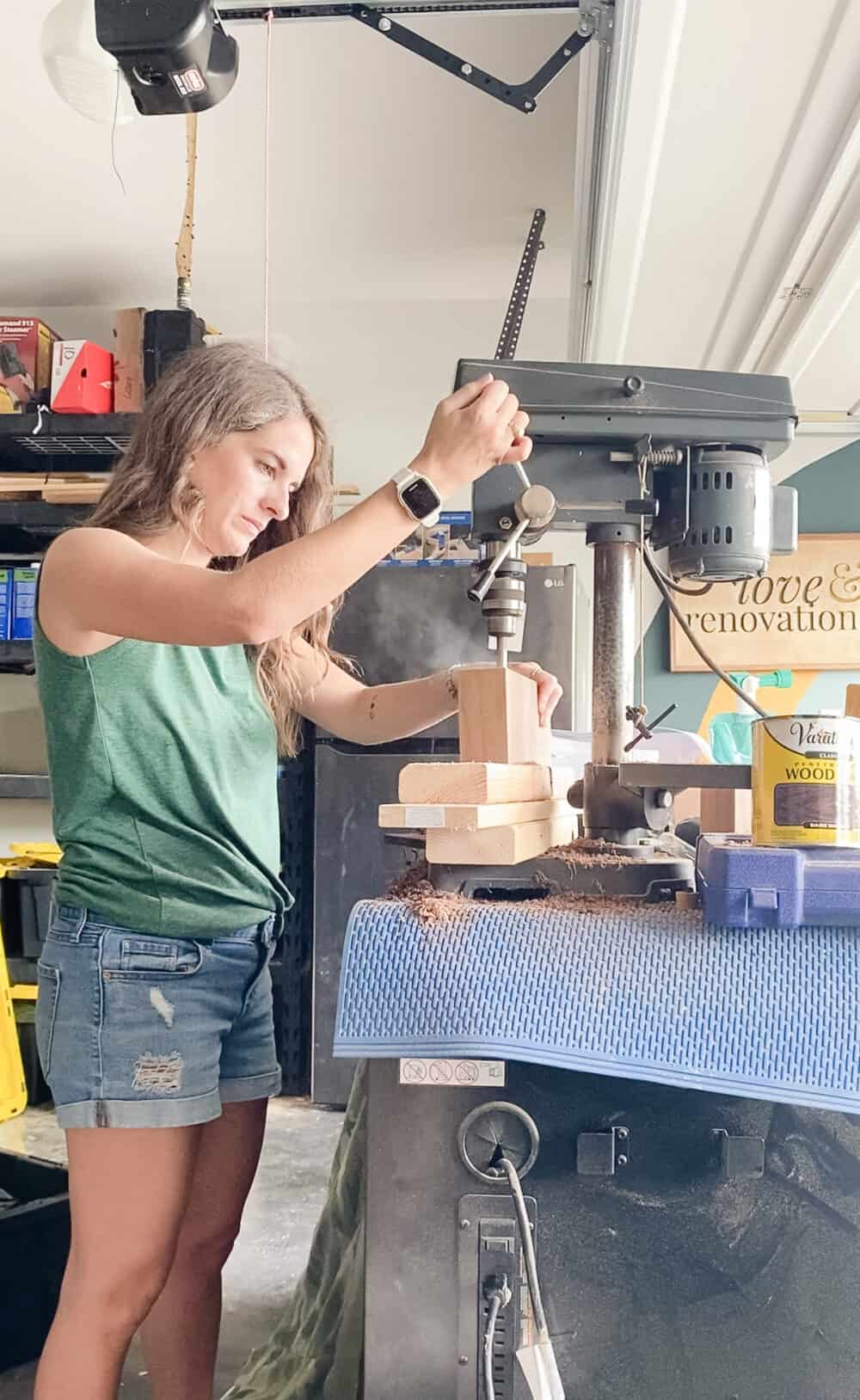 woman using a drill press to drill holes in a piece of walnut 