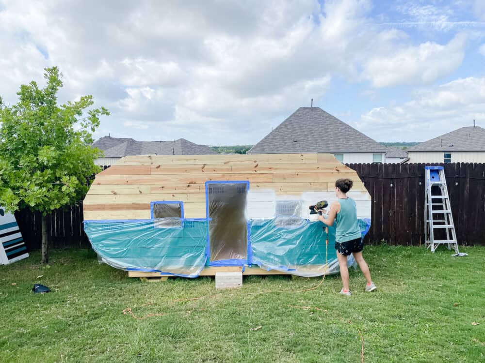 Woman painting a play camper with a paint sprayer