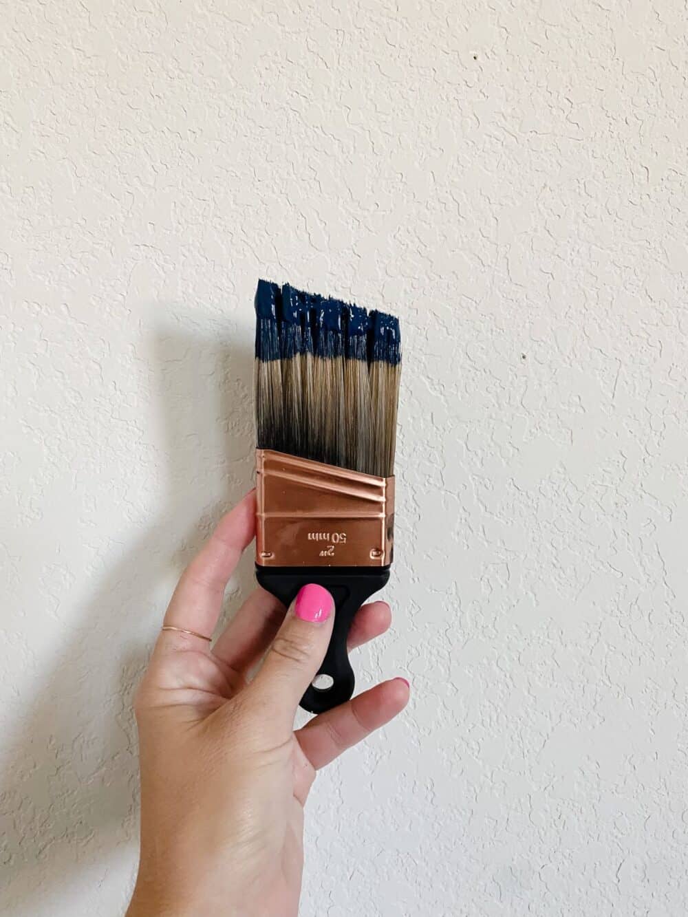 Woman's hand holding a paint brush with navy blue paint on it 