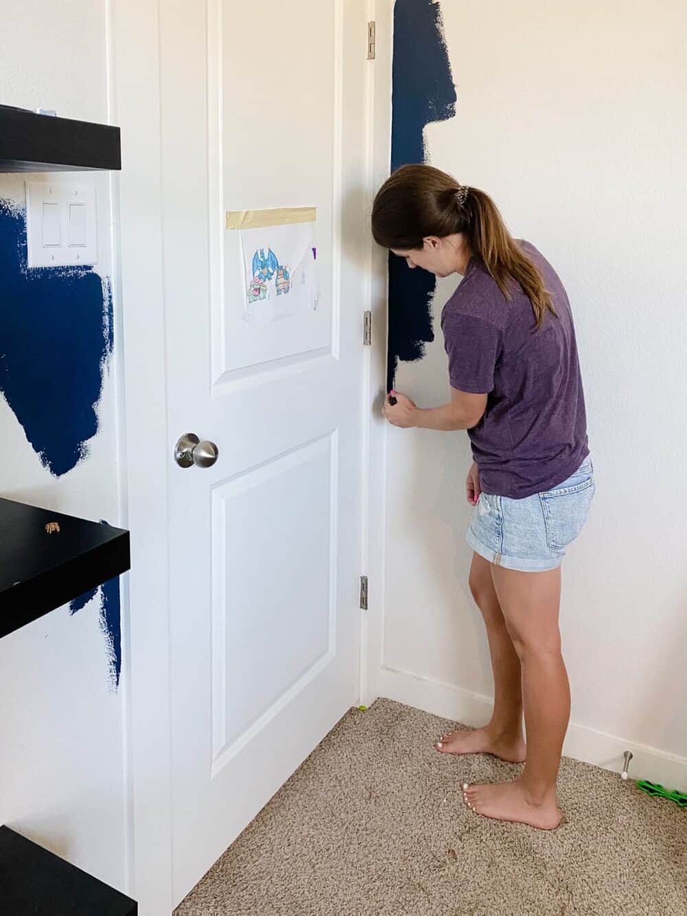 woman cutting in navy blue paint around door trim 