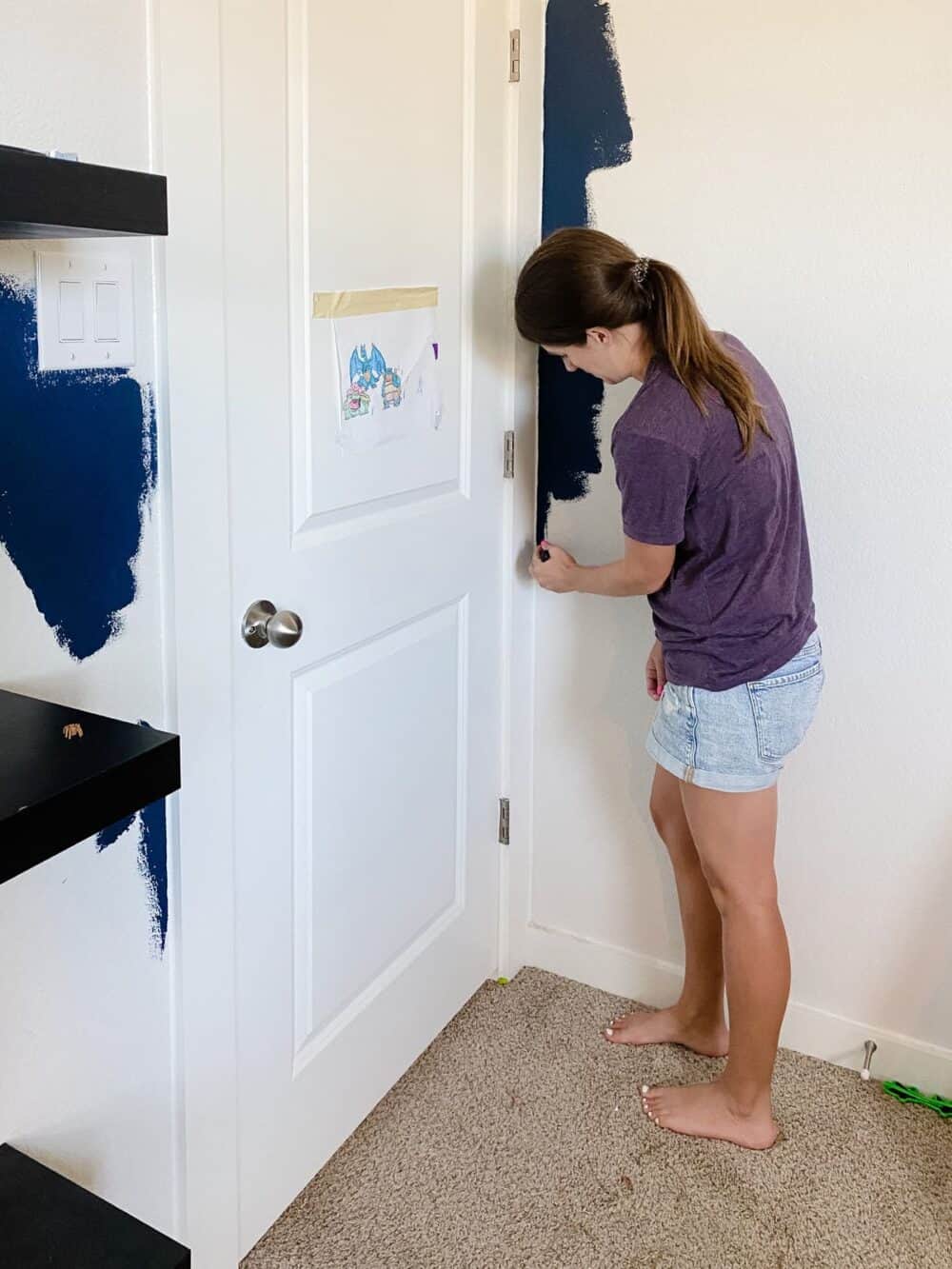 woman cutting in navy blue paint around door trim