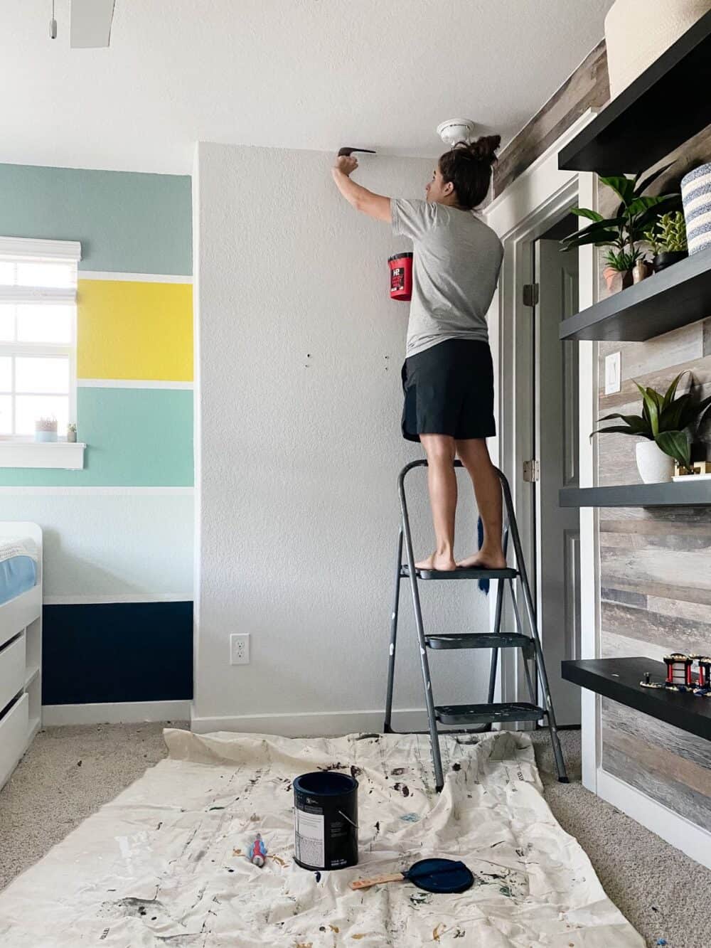 Woman cutting in edges around ceiling to paint ceiling