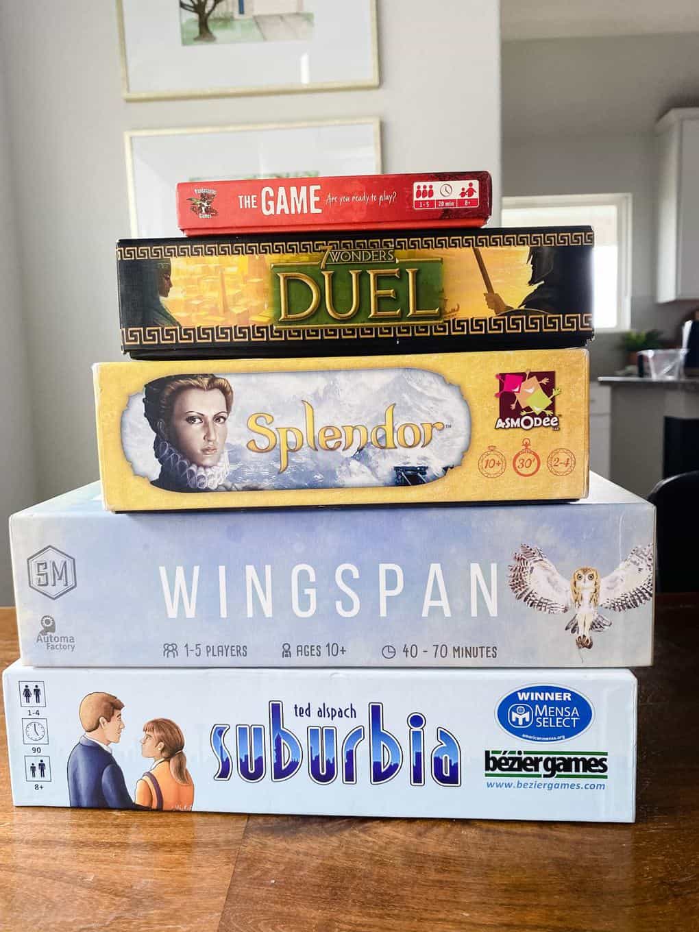Stack of board games, including Suburbia, 7 Wonders Duel, The Game, Wingspan, and Splendor