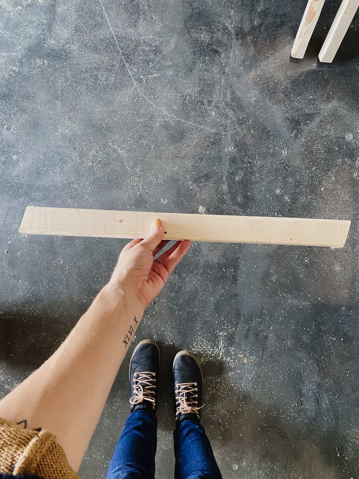 Woman's hand holding a piece of 2x2 lumber for a DIY bench