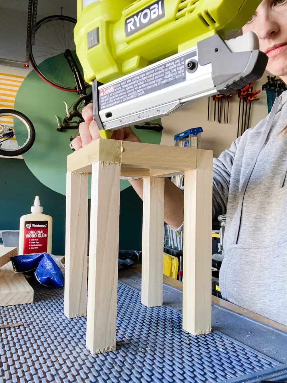 woman using a nail gun to assemble frame for a wood lantern