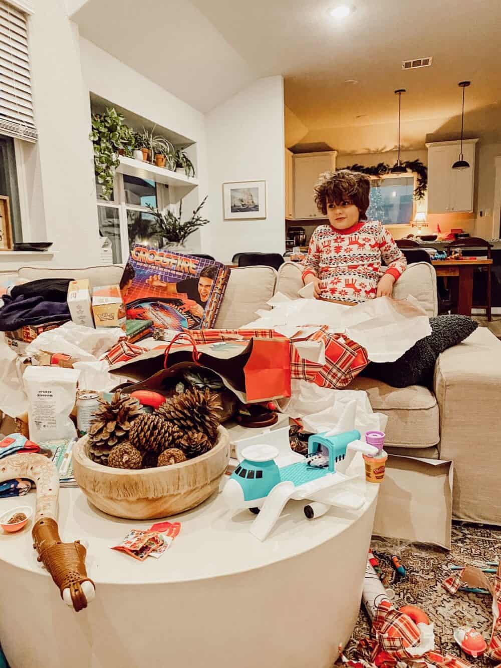 A young boy on a couch on Christmas morning surrounded by wrapping paper