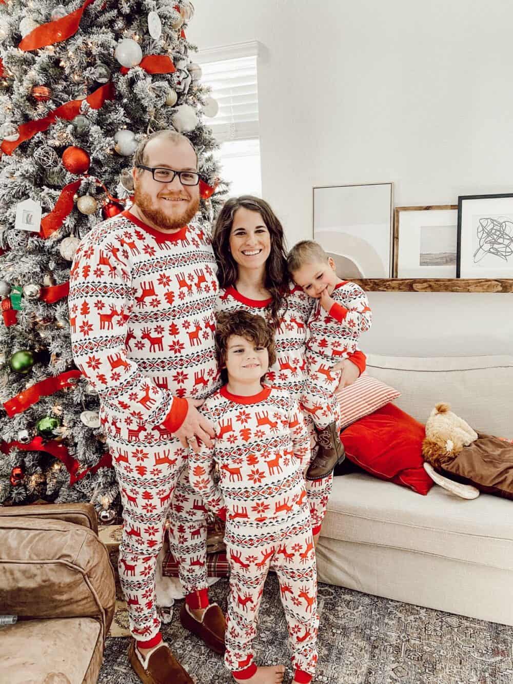 family dressed in matching Christmas pajamas standing next to a tree 