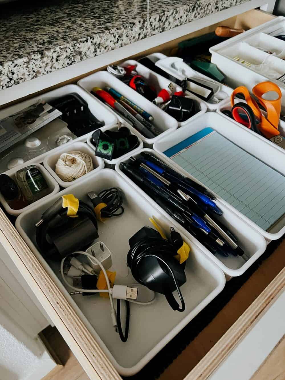 A kitchen junk drawer organized with plastic containers 
