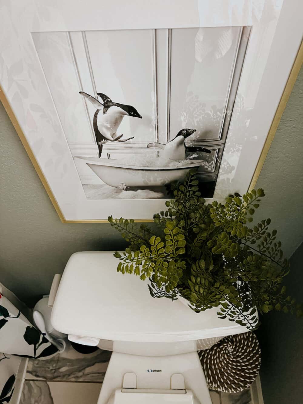 Overhead shot of a toilet with art above it and a faux plant