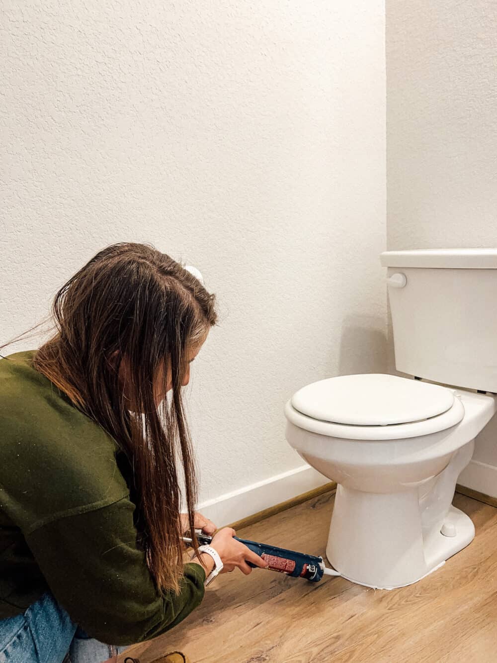 Woman caulking around a toilet