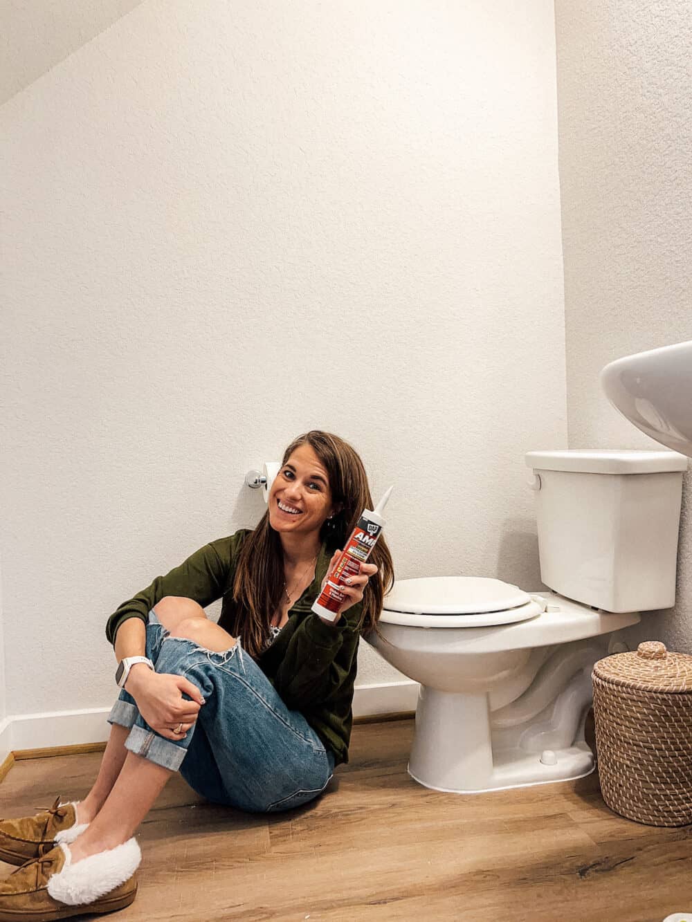 woman sitting in a bathroom holding a tube of DAP AMP kitchen and bath caulk