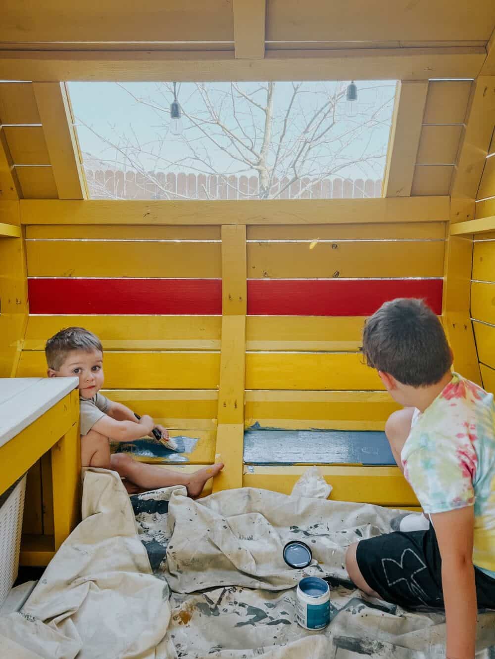 Two young boys painting in a playhouse