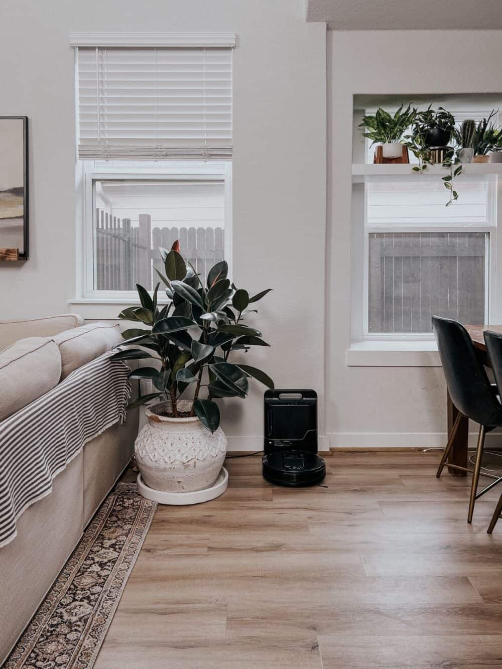 Area between an open living and dining room with a Shark robot vacuum docked near the wall 