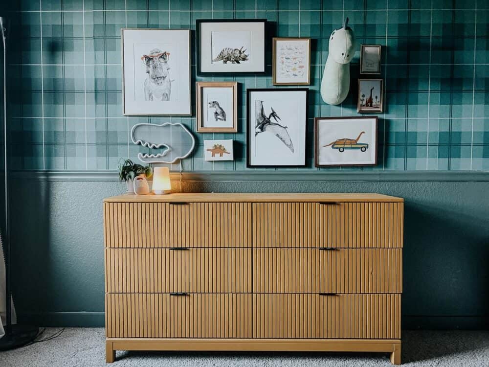 Green room with plaid wallpaper and a dinosaur gallery wall hanging above a yellow dresser 