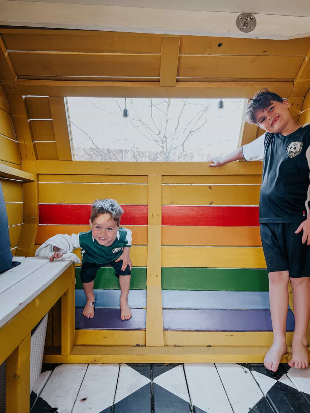 Two young boys standing in front of a rainbow stripe on a camper