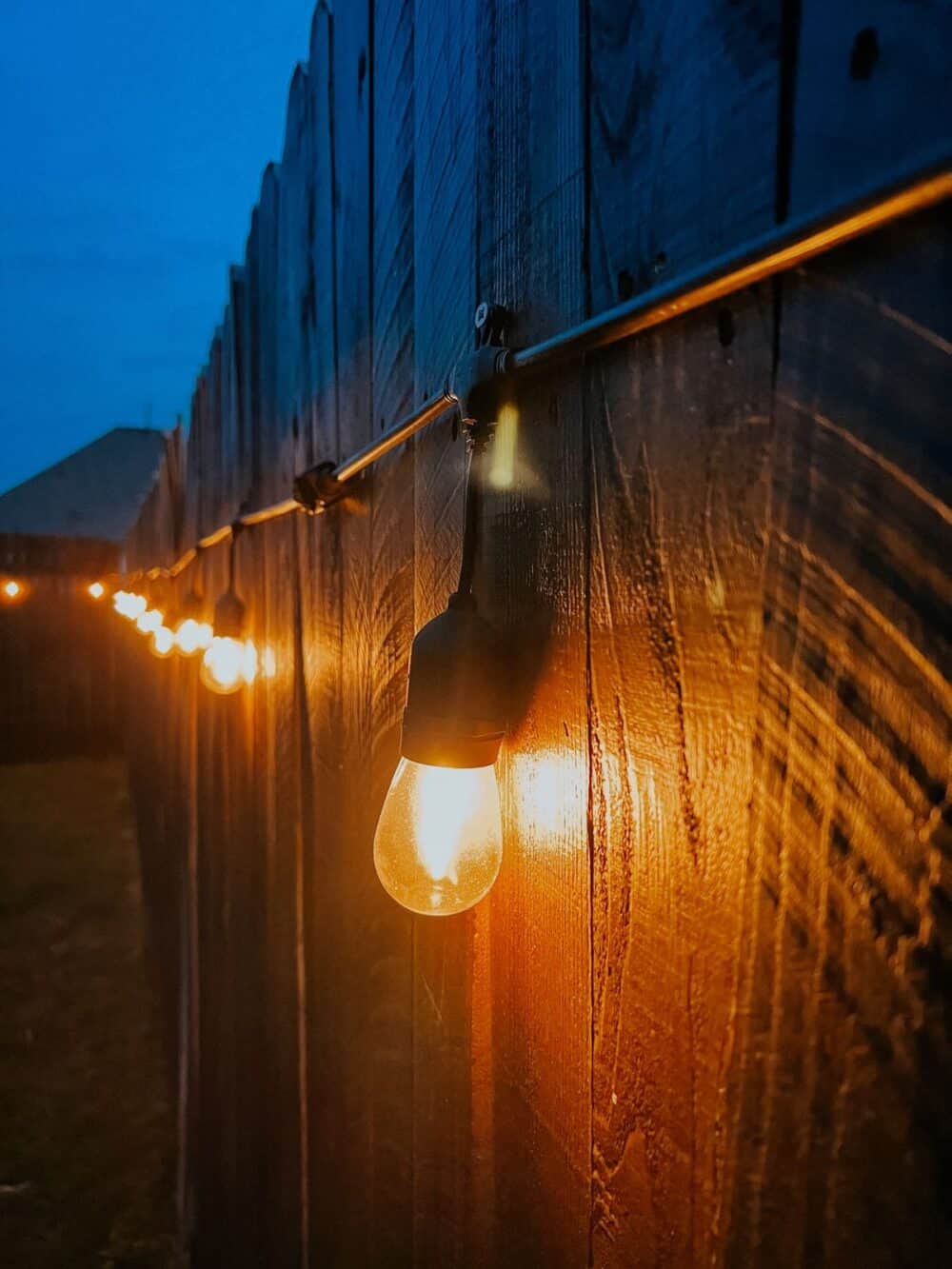 Close up of string lights on a backyard fence, attached with screws 