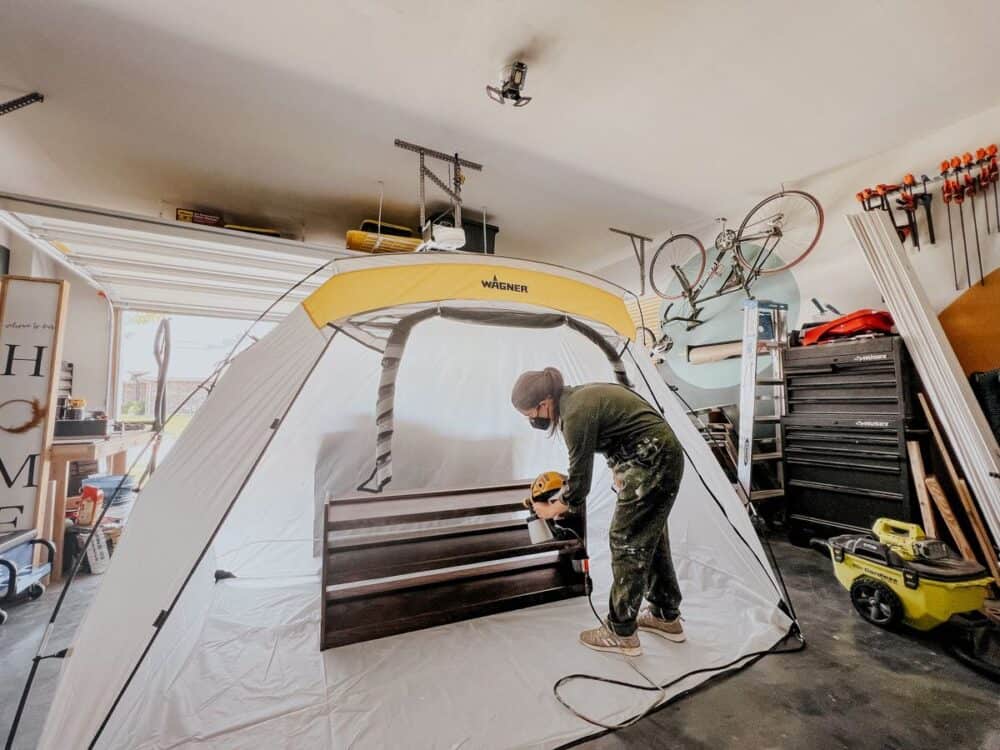 woman spraying a piece of furniture in a spray paint shelter