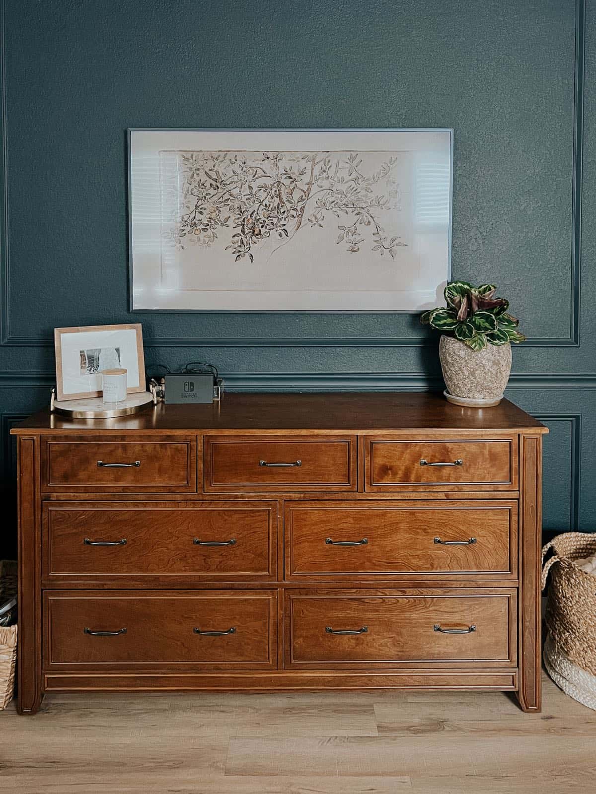 Bedroom with dark blue walls and a Frame TV hanging above a dresser 