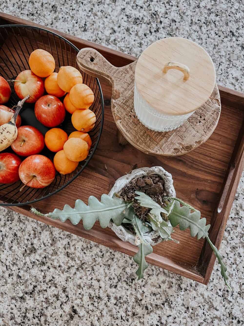 Overhead view of a tray holding a fruit bowl, a planter, and a wood pedestal with a small candle on it 