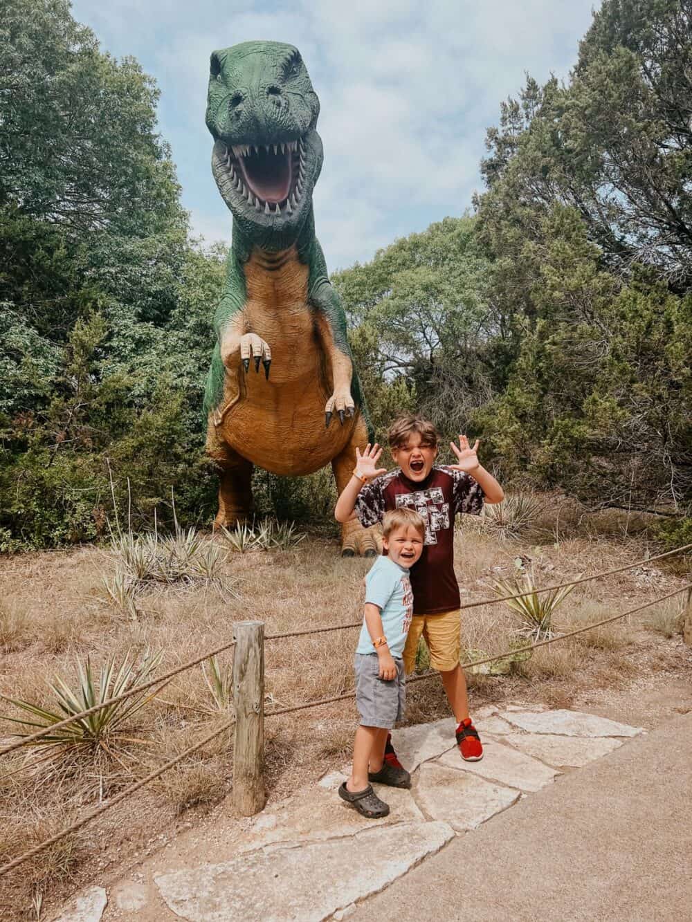 Two young boys standing in front of a dinosaur replica at Dinosaur World in Glen Rose
