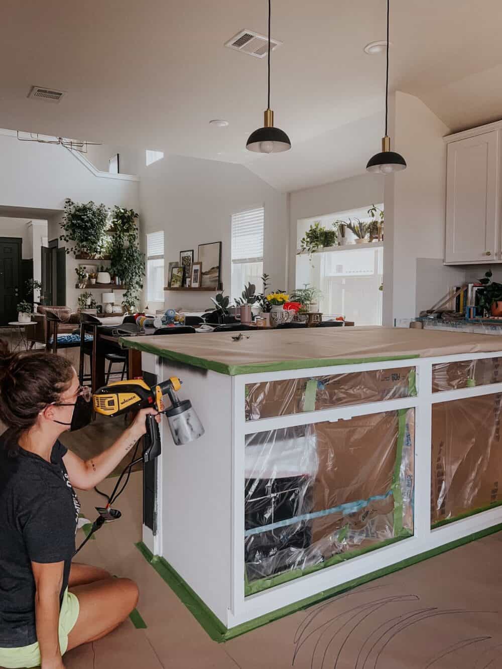 woman using a paint sprayer to paint a kitchen island black 