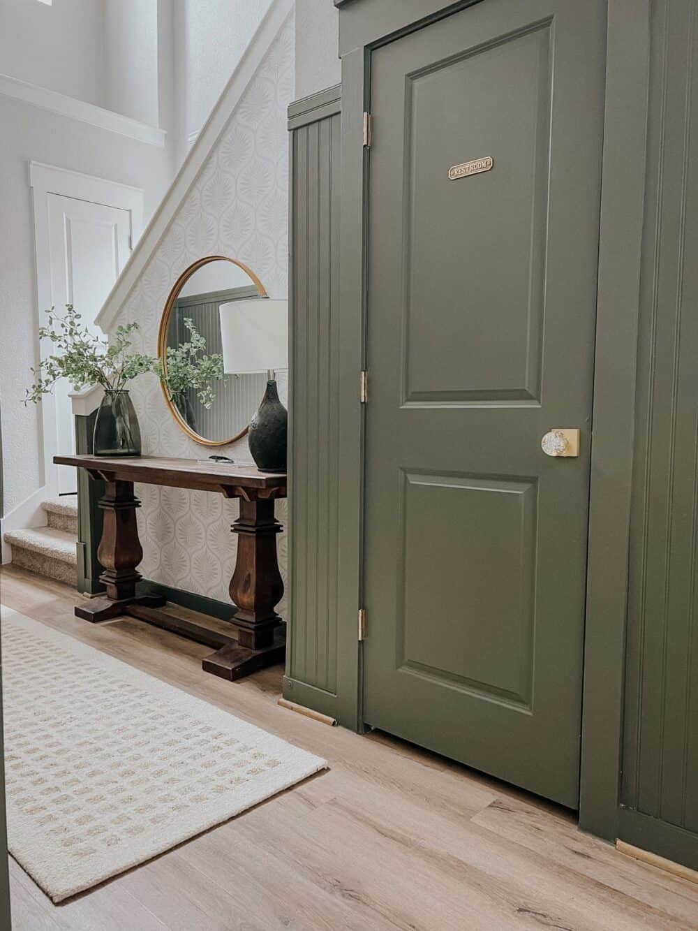 entry with green paneling and a netural rug and wallpaper 