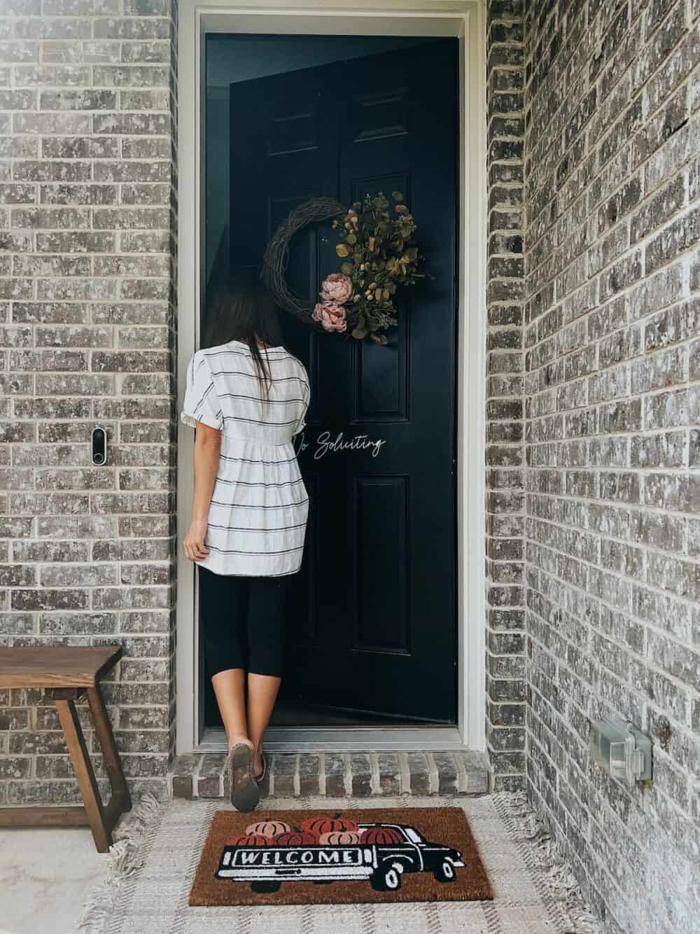woman walking into a door with a fall wreath hanging on the door 