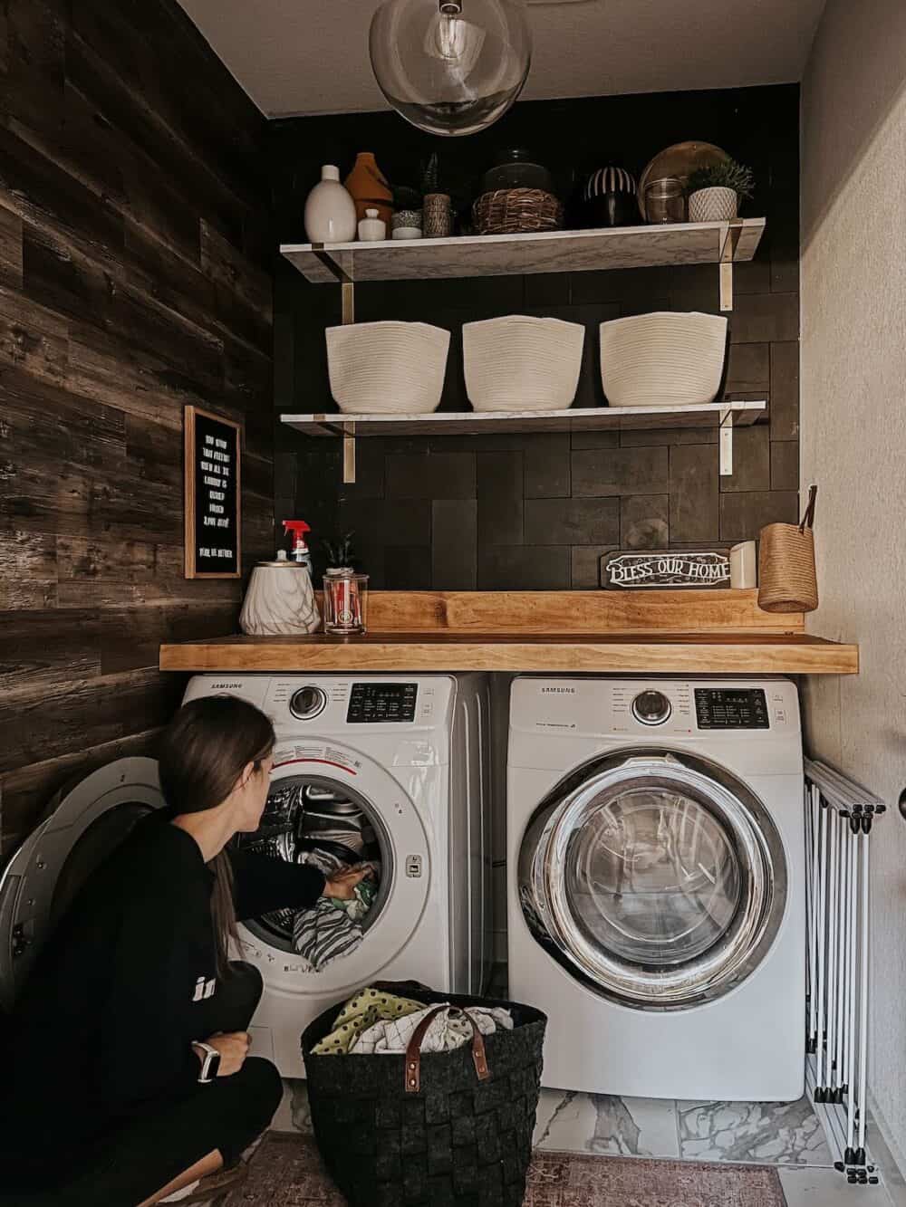 woman putting clothes in a washer in a laundry room with a wood accent wall 