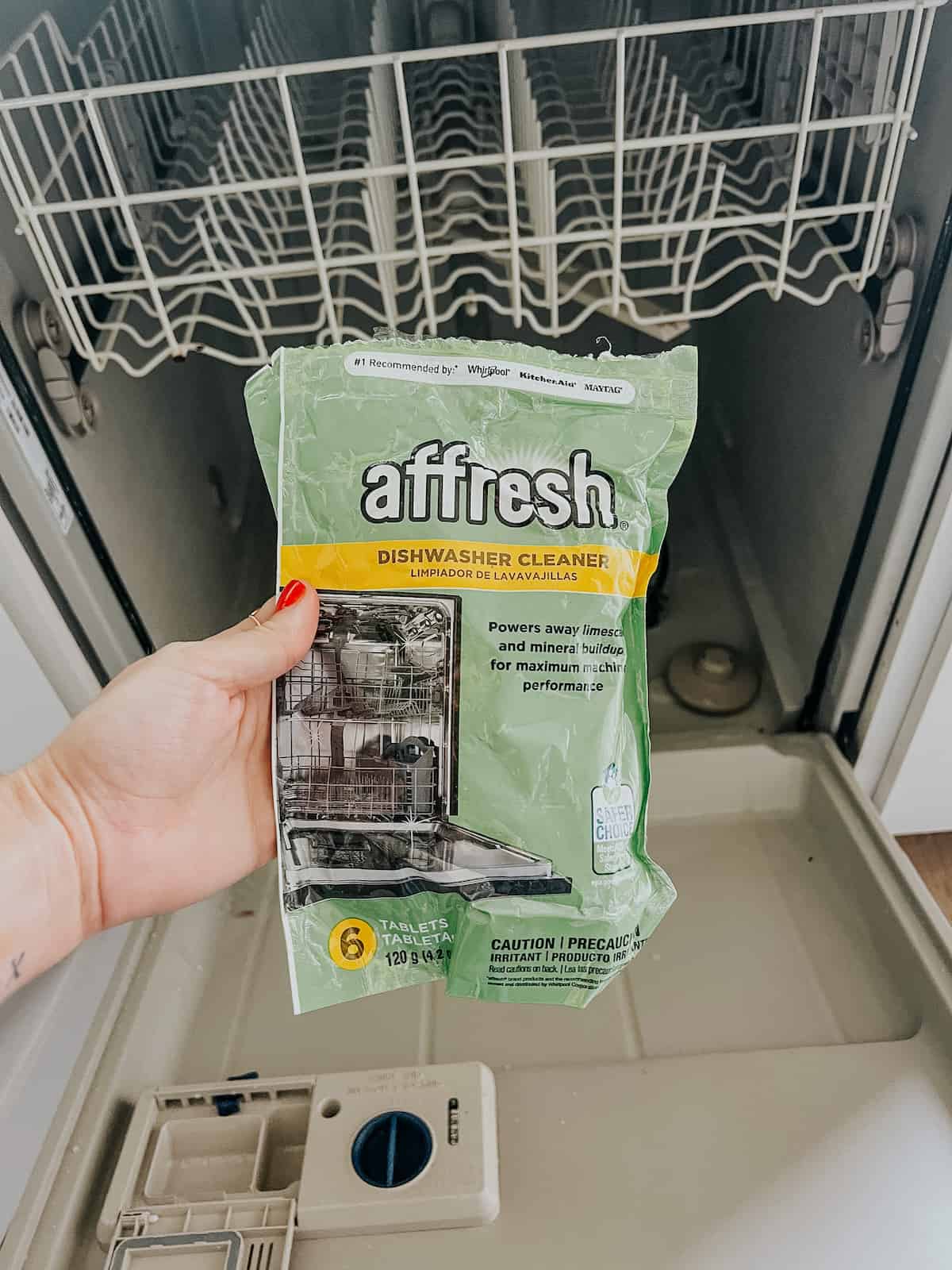 hand holding Affresh tablet in front of a dishwasher 