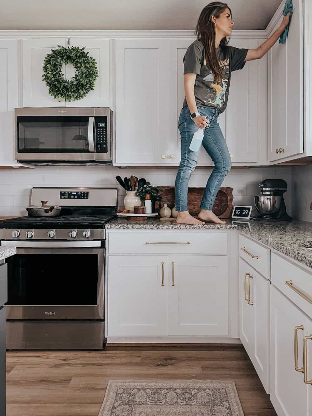 woman cleaning an upper kitchen cabinet 