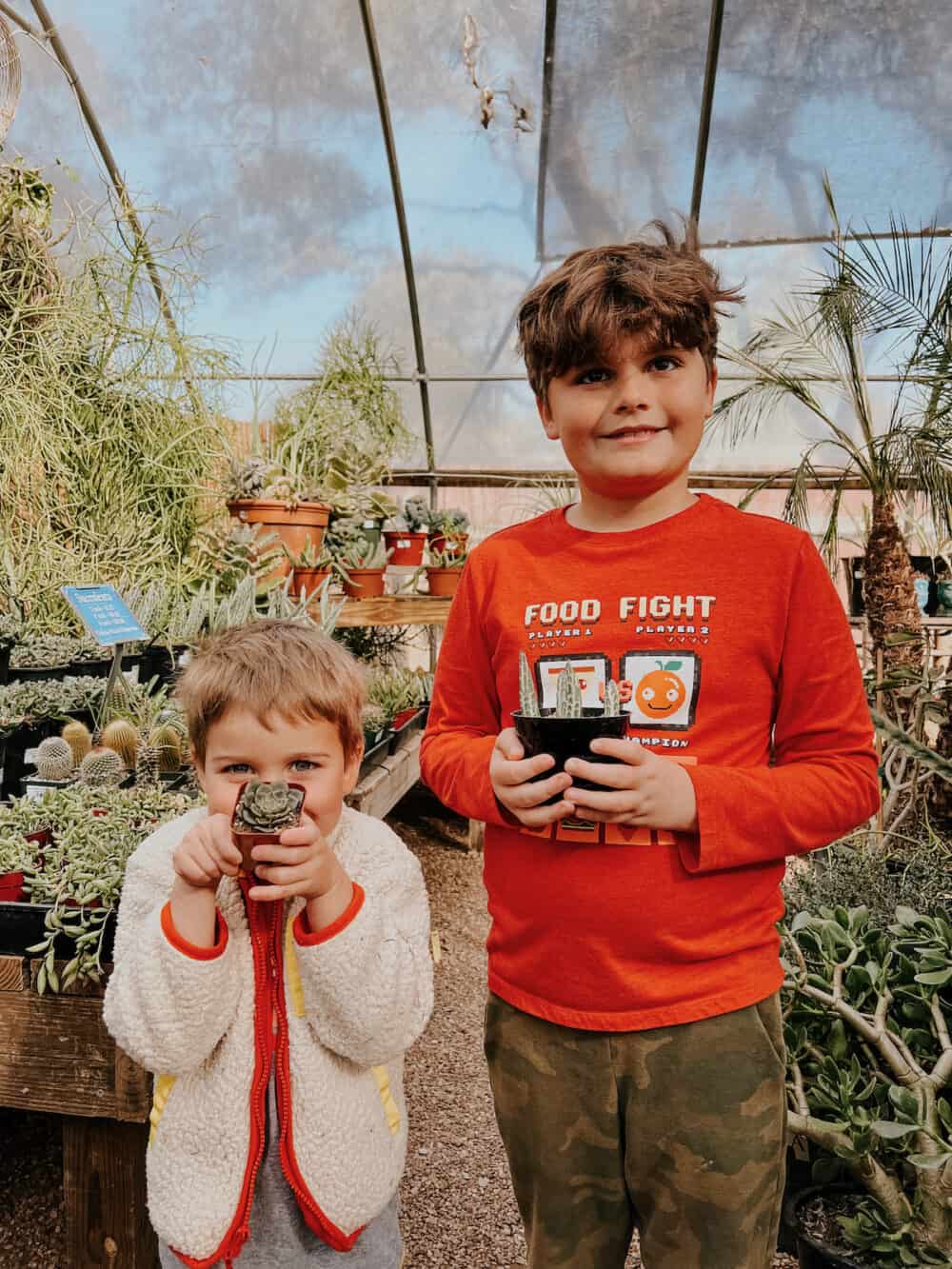 two young boys posing with plants. t a nursery 