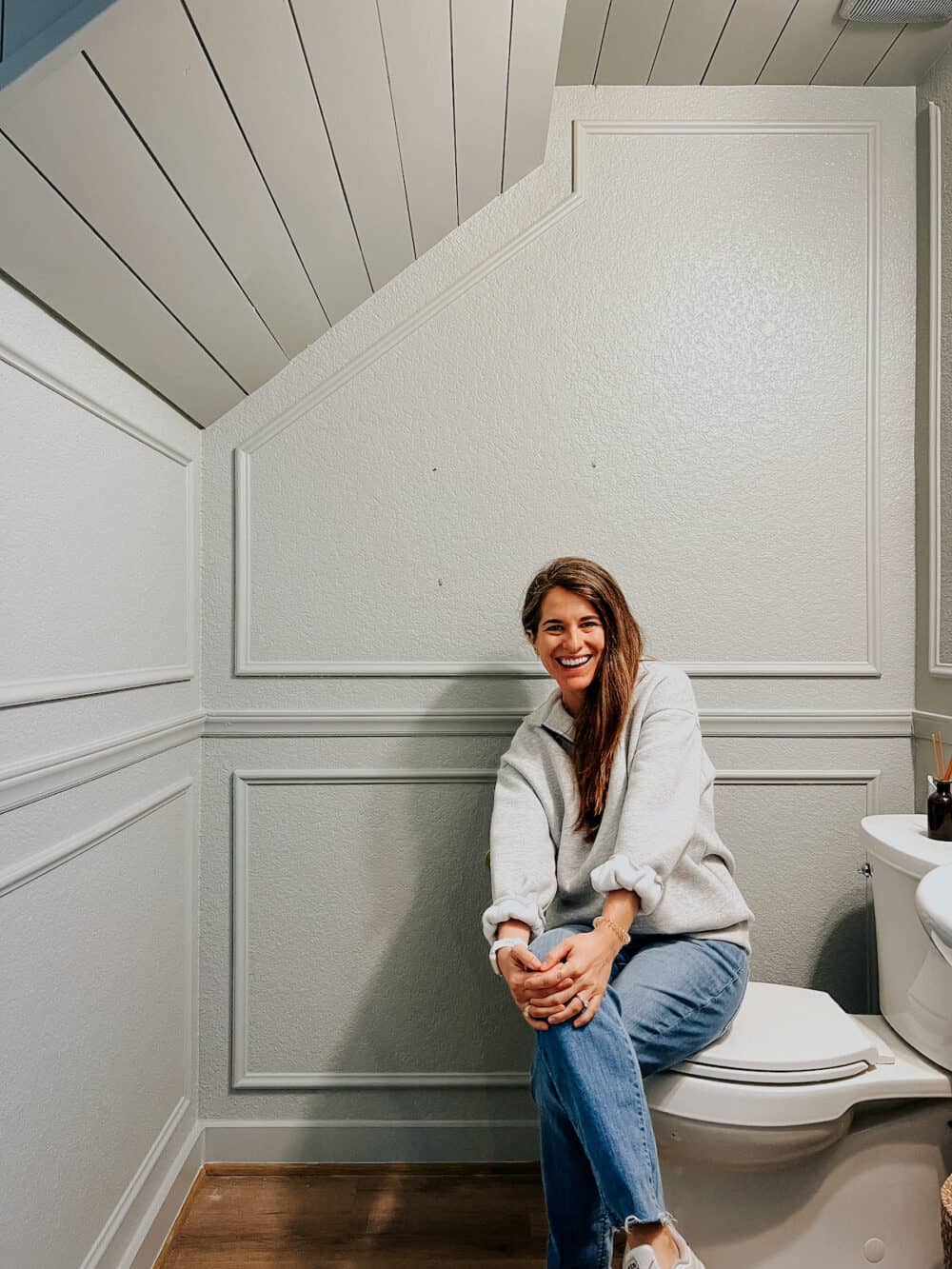 woman in a small powder room with shiplap ceiling and picture frame trim 