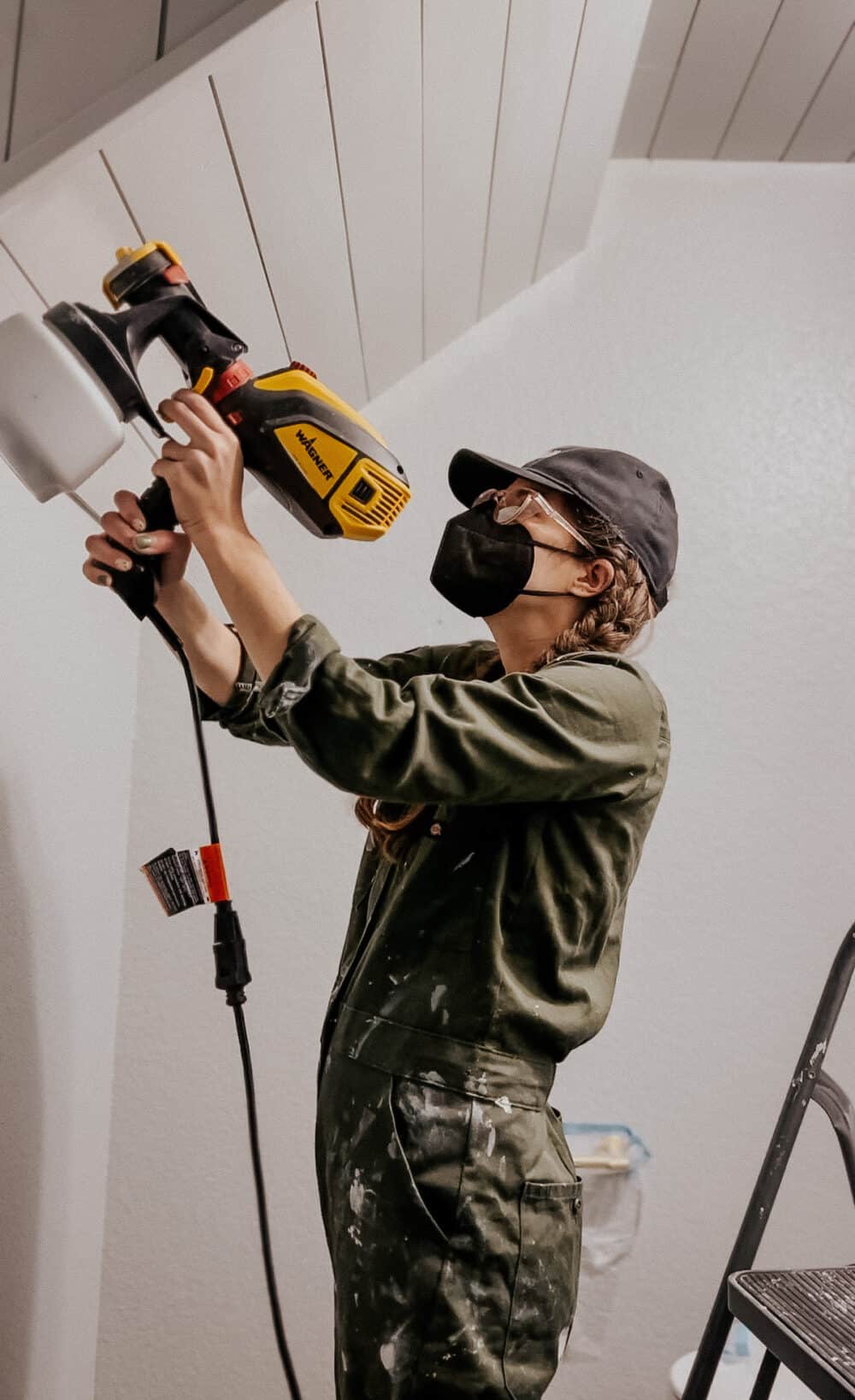 woman using a sprayer to paint a shiplap ceiling 