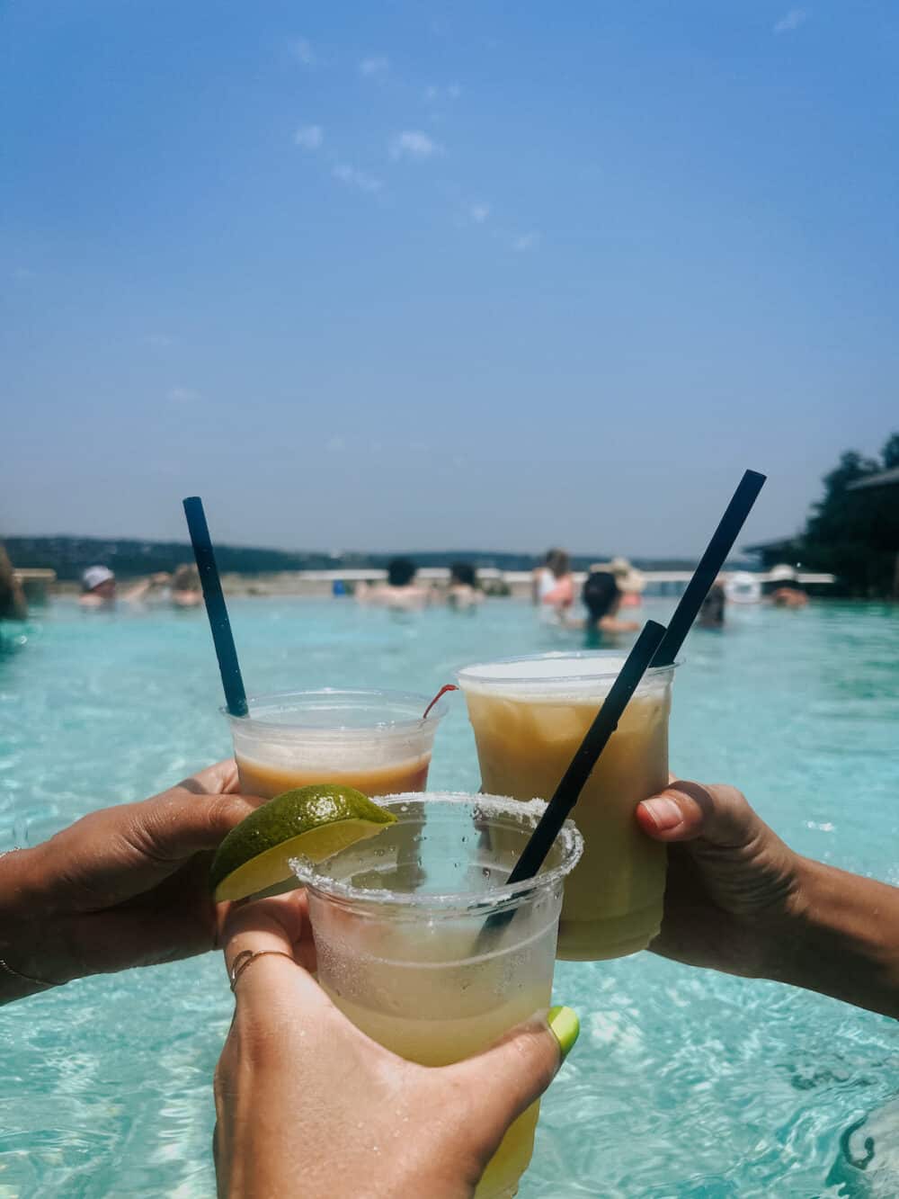 three womens' hands holding cocktails in a pool 