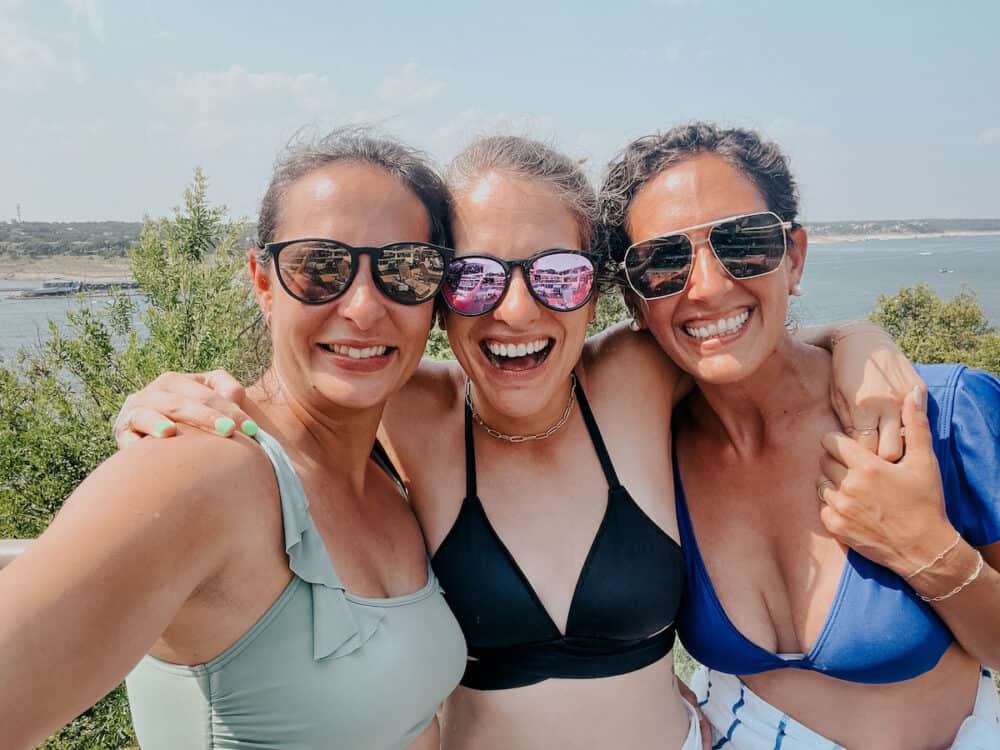 three women posing in front of a lake 