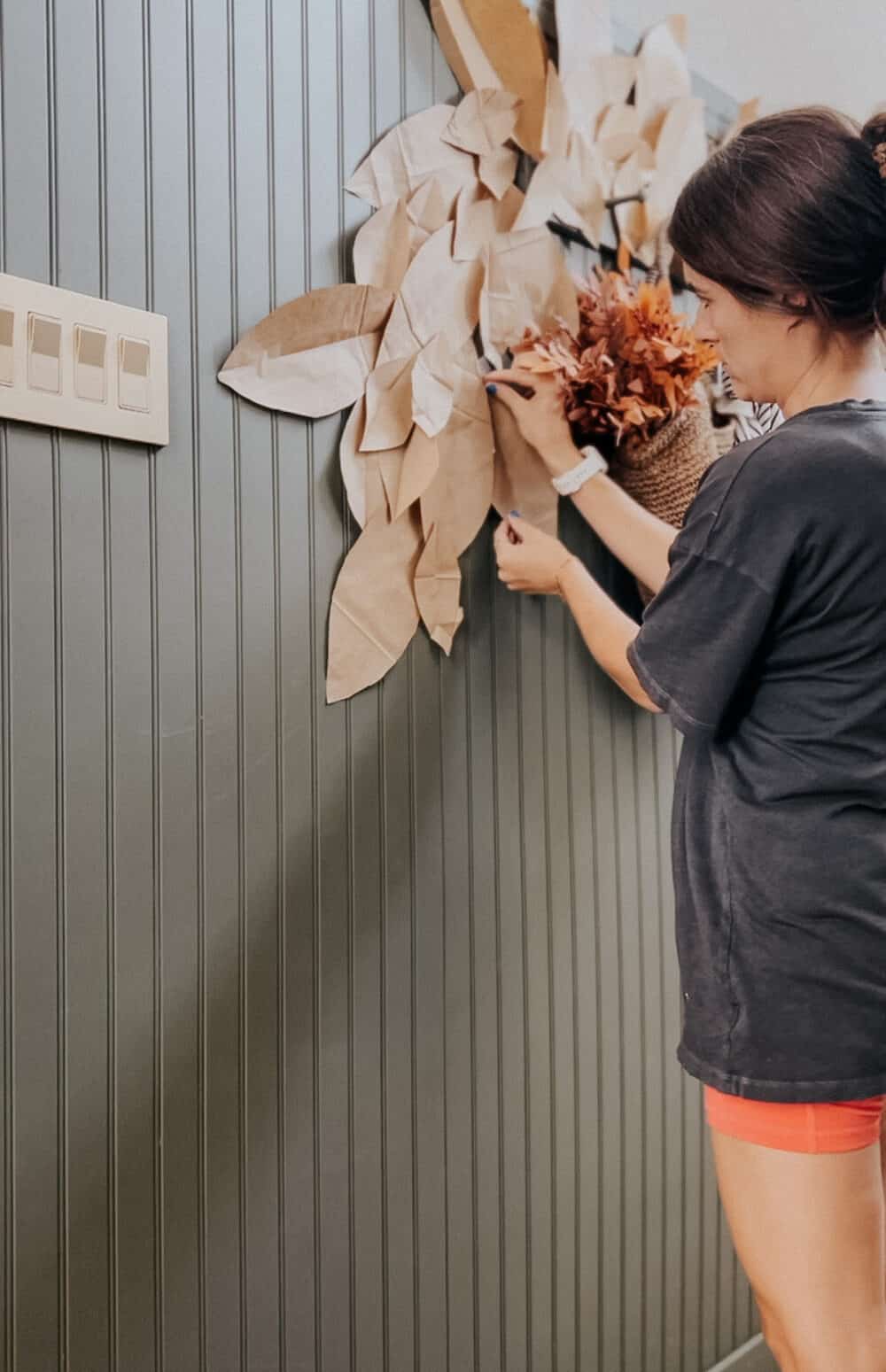 woman hanging a paper bag leaf garland on the wall