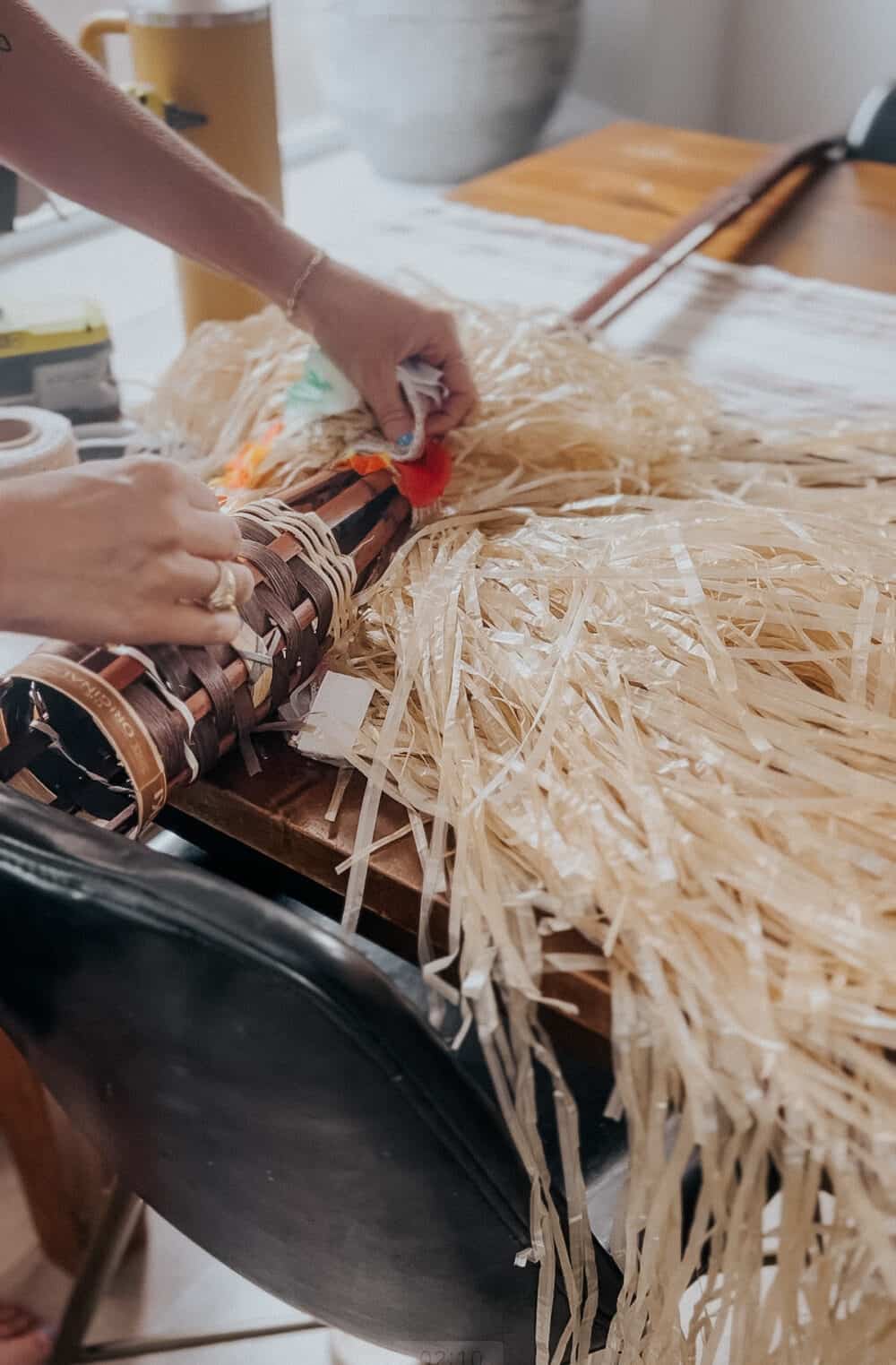 close up image of a hand attaching a grass skirt to a tiki torch to create a faux broom 