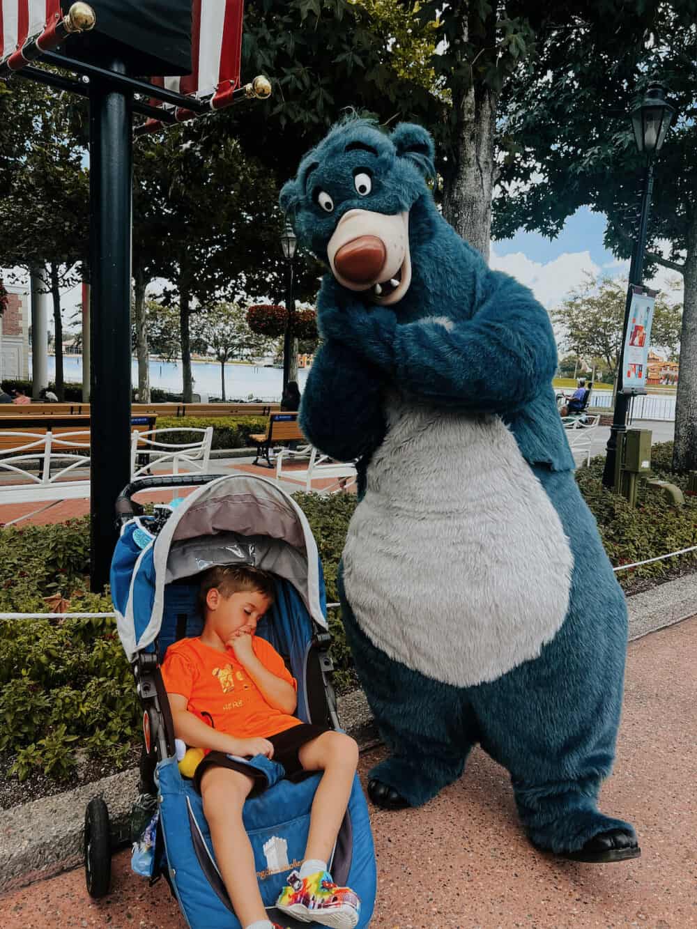 small child sleeping in a stroller next to Baloo from Jungle Book at Epcot in Disney World 