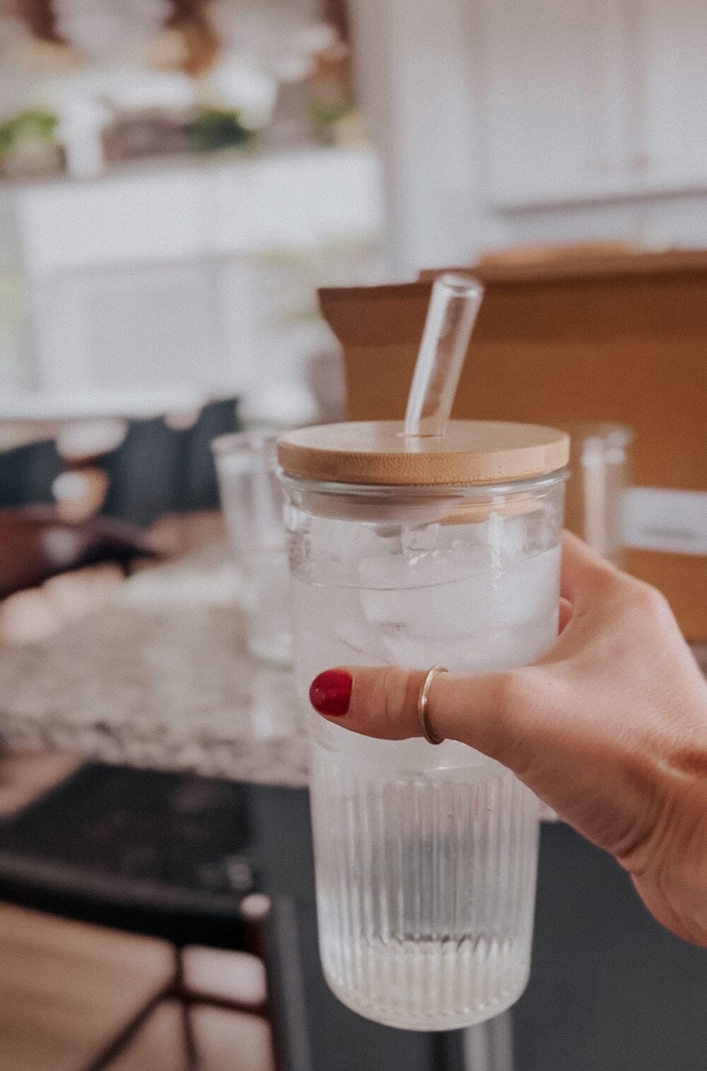 Woman's hand holding a glass tumbler with a bamboo lid and straw 