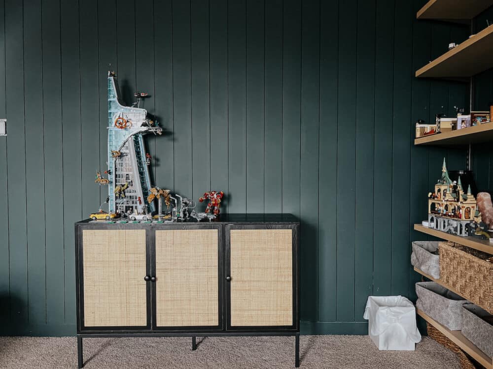 dark green painted room with a black and rattan cabinet displaying a large lego set 