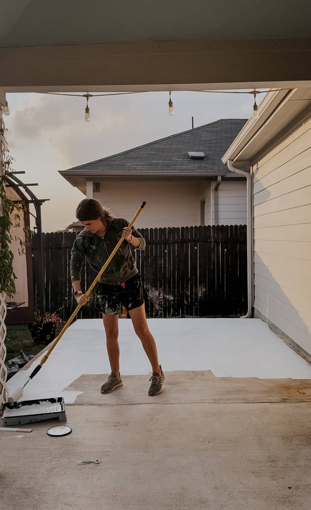 woman applying white paint to a concrete patio