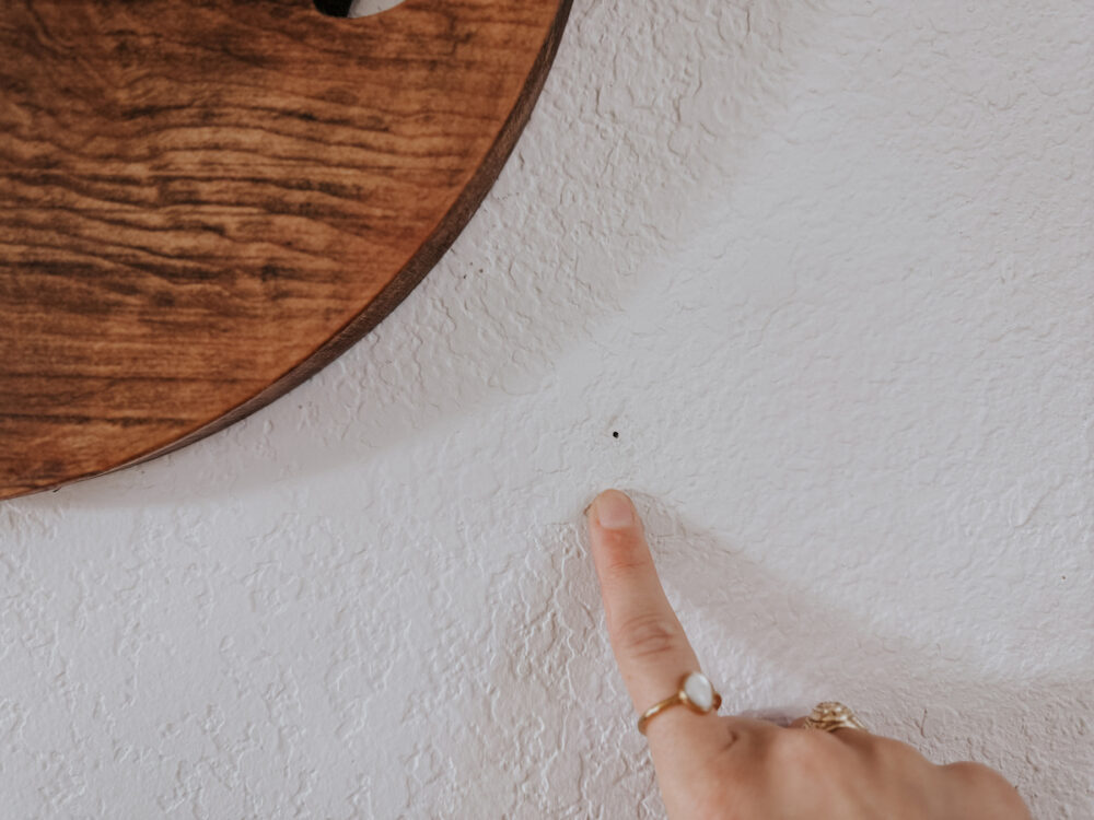 a woman pointing at a small nail hole in drywall